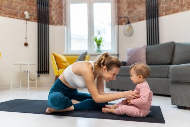 Sağlıklı gelişme. Atletik anne ve bebek evde birlikte egzersiz yapıp oturma odasında oynuyorlar..