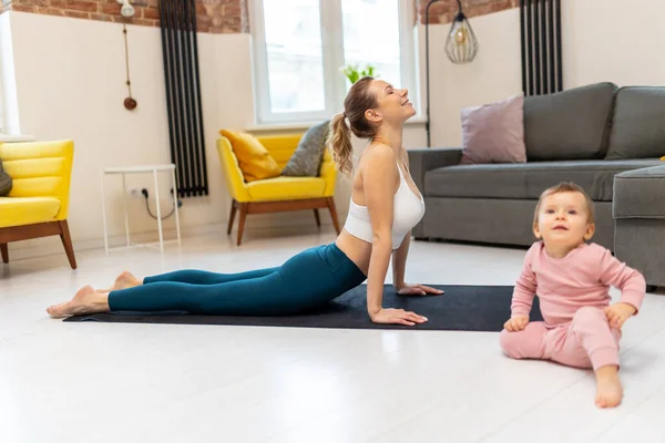 stock image Young sporty mother in sportswear and baby girl working out exercising together at home in living room.