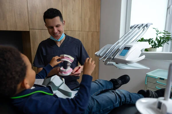 Επίδειξη Οδοντοστοιχίας Μελαχρινή Γιατρός Δείχνει Οδοντοστοιχία Στο Χαριτωμένο Μικρό Ασθενή — Φωτογραφία Αρχείου