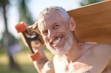 Şehirli bir parkta elinde sörf tahtasıyla gülümseyen olgun bir adam. Aktif, sağlıklı bir yaşam tarzı..