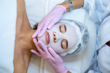 Tanımlanamayan profesyonel doktor kozmetik uzmanı müşterinin yüzüne çarşaf maskesi takıyor, estetik kliniğindeki kadın....