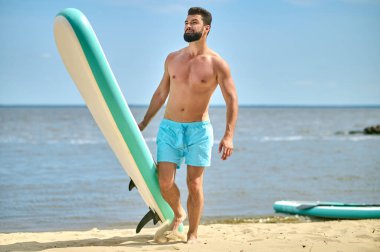 Deniz kenarındaki kumlu sahilde duran yakışıklı atletik adam, tatilin tadını çıkarıyor, aktif bir yaşam tarzı..