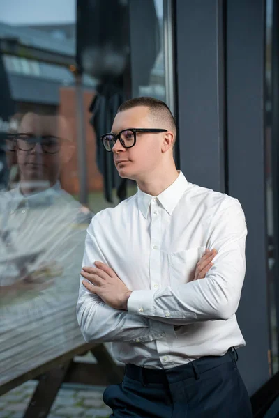 stock image Young businessman standing near window in company office, looking away. Successful man entrepreneur posing with crossed arms.