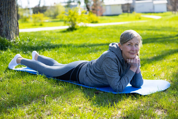 Утренняя йога. Зрелая женщина в серой спортивной машине занимается йогой в парке