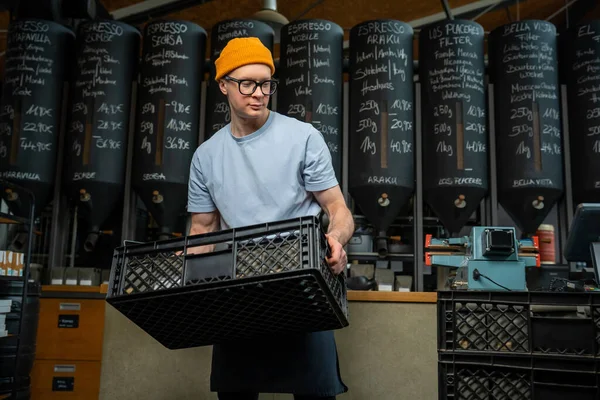 stock image Caucasian man wearing hat apron and glasses coffee shop worker gets new batch of coffee packages in boxes on roasting factory.