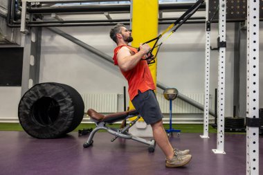 Sporcu sakallı adam spor salonundaki kaslarını güçlendirmek için spor aletleriyle egzersiz yapıyor..