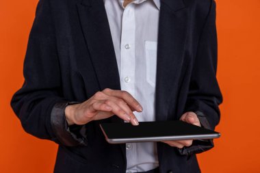 Turuncu arka planda izole edilmiş tablet kullanan siyah takım elbiseli tanınmayan bir kadın..