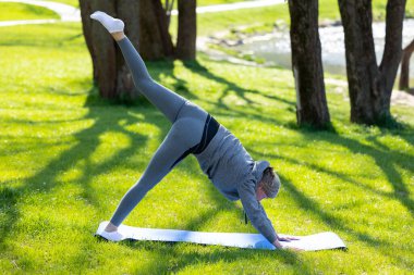 Sabah yogası. Gri spor kıyafetli kadın parkta yoga yapıyor.