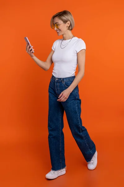 穿着白色T恤和牛仔裤的女性博客作者使用智能手机浏览互联网 — 图库照片