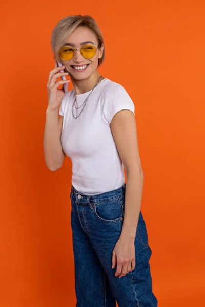 Tevreden Vrouw Wit Shirt Jeans Praten Mobiele Telefoon Geïsoleerd Oranje — Stockfoto