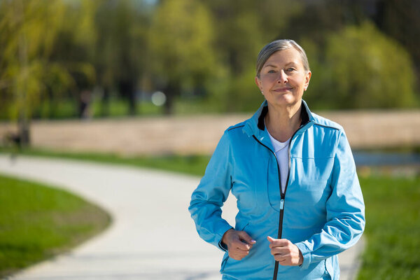 Running in the park. Mature good-looking woman running in the park and looking contened