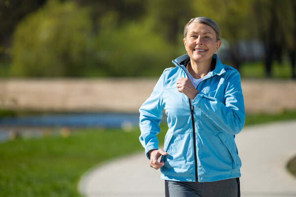 Running in the park. Mature good-looking woman running in the park and looking contented