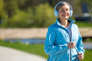 Sabah koşusu. Parkta koşan mavi ceketli, gülümseyen kadın.