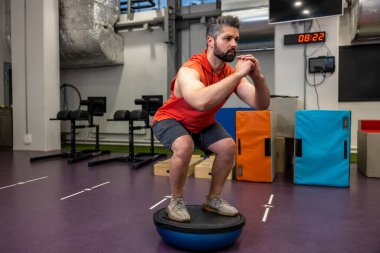 Formda sporcu spor salonunda jimnastik yarı küre bosu topu üzerinde egzersiz yapıyor ve mekik çekiyor..