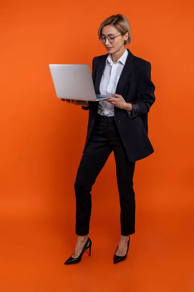 自信に満ちた女性起業家黒公式スタイルのスーツを着てノートブック上で作業オレンジの背景に孤立 — ストック写真