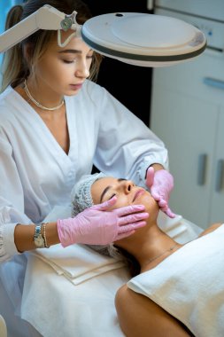Genç kadın kozmetik uzmanı kadınların yüzüne beyaz maske takıyor. Güzellik salonu spa prosedürleri..