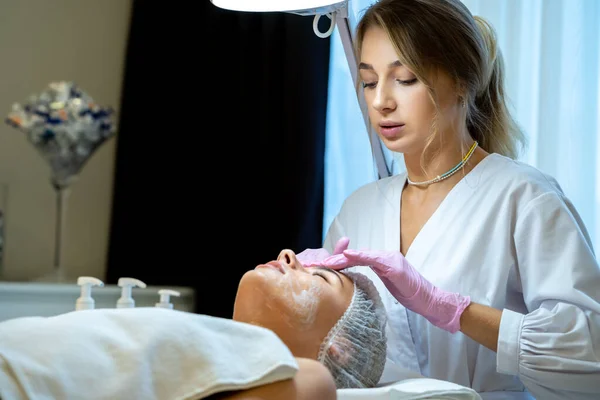 Ξανθιά Γυναίκα Cosmetologist Εφαρμογή Λευκή Μάσκα Γυναίκες Πρόσωπο Αισθητική Κλινική — Φωτογραφία Αρχείου