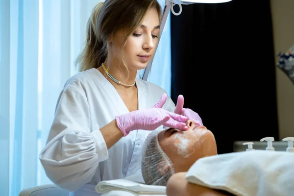 Νεαρή Γυναίκα Cosmetologist Εφαρμογή Λευκή Μάσκα Γυναίκες Πρόσωπο Σαλόνι Ομορφιάς — Φωτογραφία Αρχείου
