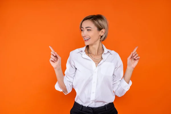 喜びの女性は オレンジの背景に隔離されたスペースをコピーするために両側を指す白い公式スタイルのシャツを着て — ストック写真