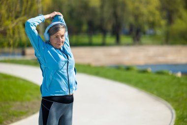 Sabah egzersizleri. Spor giyimli orta yaşlı bir kadın parkta egzersiz yapıyor.