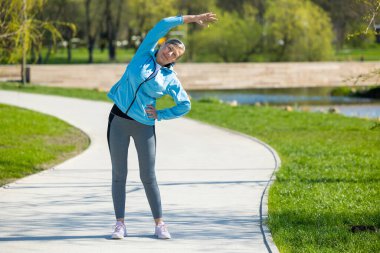 Esniyorum. Spor kıyafetli kadın parkta esneme hareketleri yapıyor.