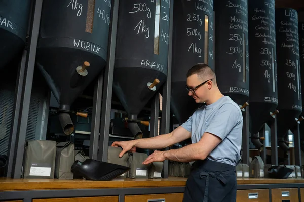 咖啡店的店员戴着眼镜 围裙站在柜台旁倒咖啡豆 — 图库照片