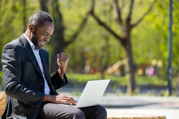 在外面工作在公园里的笔记本电脑上工作的非裔美国商人看上去很满意 — 图库照片