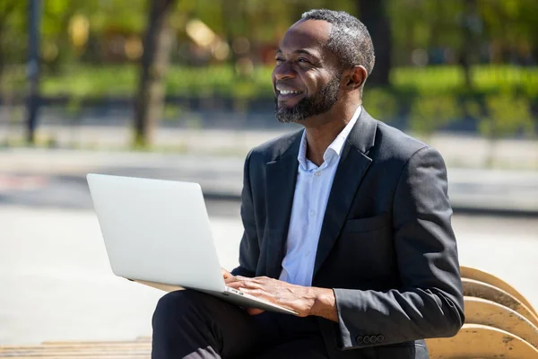 在外面工作在公园里的笔记本电脑上工作的非裔美国商人看上去很满意 — 图库照片