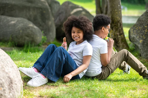 两个穿着白色T恤衫在公园里吃冰激凌的孩子坐在绿草上 — 图库照片