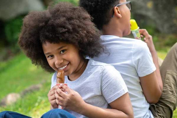 两个穿着白色T恤衫在公园里吃冰激凌的孩子坐在绿草上 — 图库照片