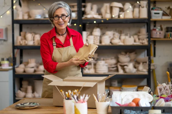 顧客の注文を梱包し 紙に包装する陶器店のシニア女性販売業者または労働者 — ストック写真