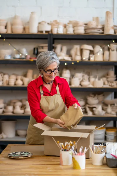 客户的陶瓷商店高级女销售员或女工包装定单并将其包装成纸 — 图库照片
