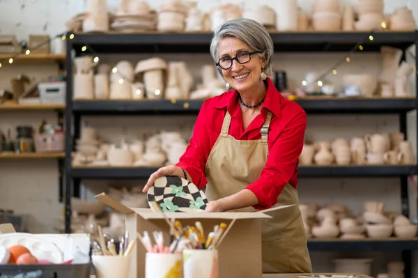 顧客の注文を梱包し 紙に包装する陶器店のシニア女性販売業者または労働者 — ストック写真