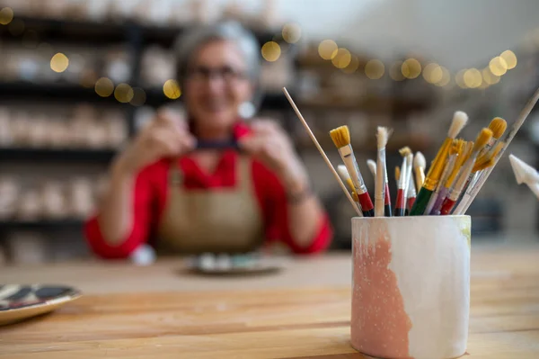 Pędzle Malowania Stole Niewyraźnym Mistrzem Ceramiki Kobieta Fotografująca Wyniki Pracy — Zdjęcie stockowe