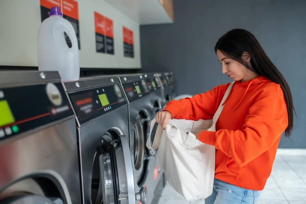 洗濯室の洗濯機に汚れた服を挿入するブルネットの女性 — ストック写真