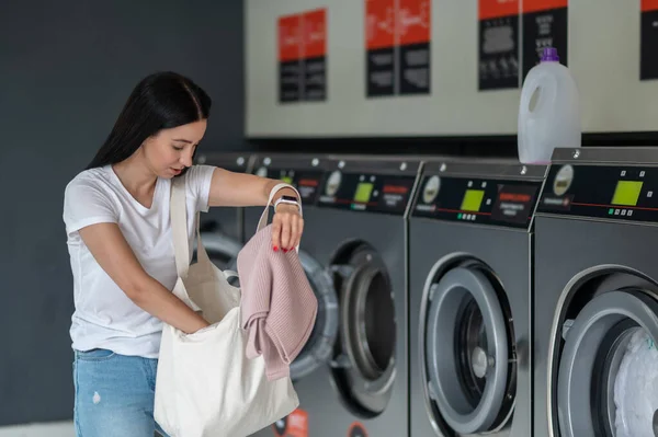 洗濯室の洗濯機に服を卸しているブルネットの女性 — ストック写真