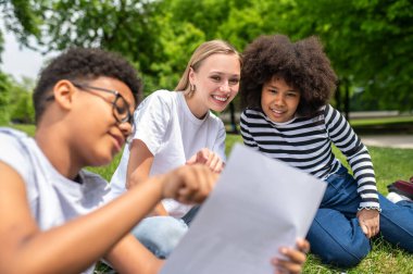 Birliktelik. Sarışın gönüllü çimde oturuyor ve çocuklara testlerde yardım ediyor.