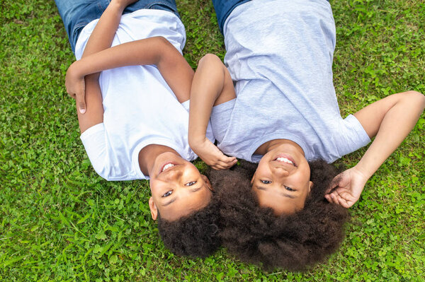 Top view of cute little boy and girl smiling while lying the grass in park.