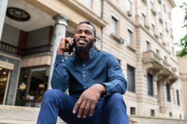 Telefonlu adam. Koyu tenli, kot elbiseli, elinde telefon olan bir genç.