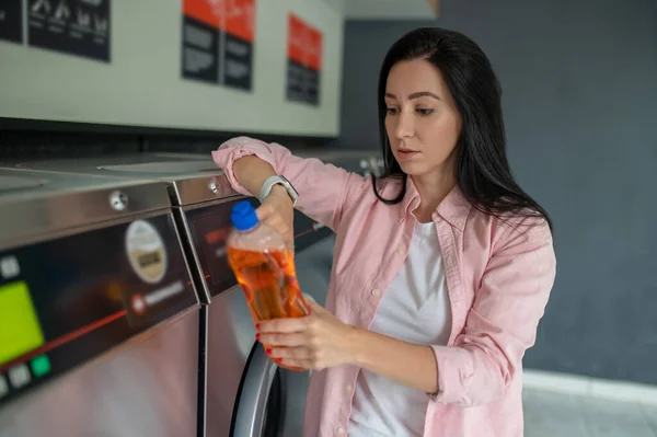 stock image Brunette woman in laundromat showing cleaning detergent.