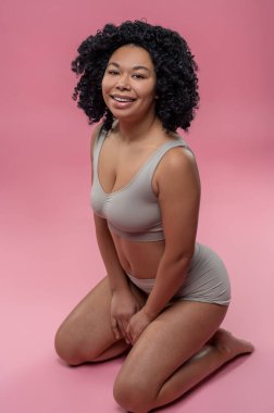 Temyize git. Güzel kıvırcık saçlı kadın iç çamaşırlarıyla yerde oturuyor.