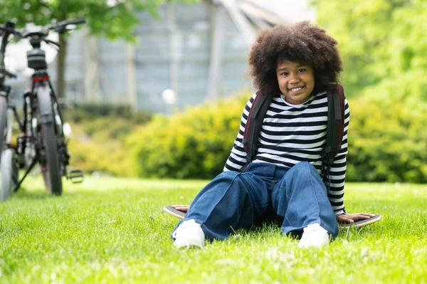 Счастливая Маленькая Африканская Американка Полосатой Рубашке Джинсах Сидящая Траве Парке — стоковое фото