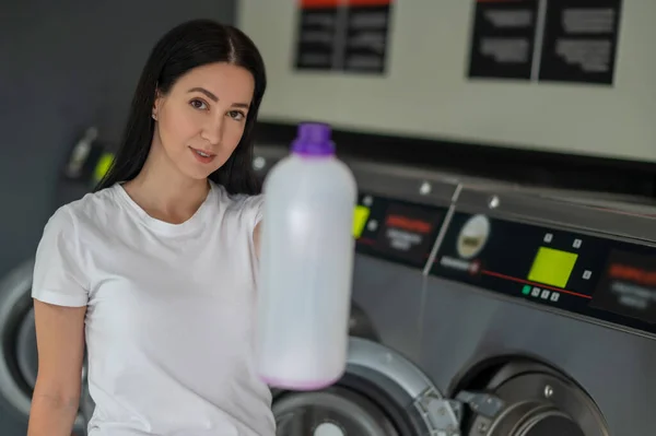 stock image Young woman holding detergent using washing machine in public laundry.