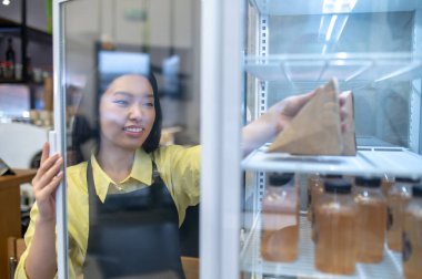 - Kafede. Önlüklü genç kız buzdolabından yiyecek alıyor.