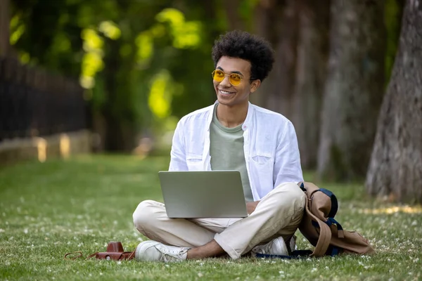 stock image Digital nomad. Young curly-haired man working on laptop in the park