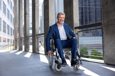Gülümseyen gri saçlı engelli adam tekerlekli sandalye şehrinin arka planında resmi bir takım elbise giyiyor..