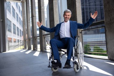 Tekerlekli sandalyede resmi stil kıyafet giyen mutlu gri saçlı adam, kollarını kaldırdı, yumruklarını sıktı, başarısını kutladı..