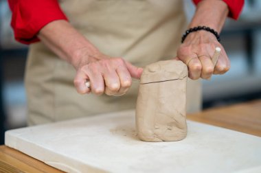Çömlekçilikte elle yoğurma tekniği. Tanımlanamayan bir kadın stüdyoda masanın arkasında iplikle kil kesiyor..