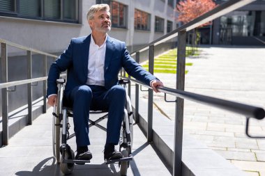 Beyaz saçlı, resmi giysili, yetişkin iş adamı tekerlekli sandalye rampasında çalışıyor..