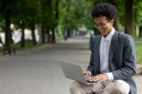 Digitális Nomád Göndör Hajú Mosolygós Fiatalember Aki Laptopon Dolgozik Parkban — Stock Fotó